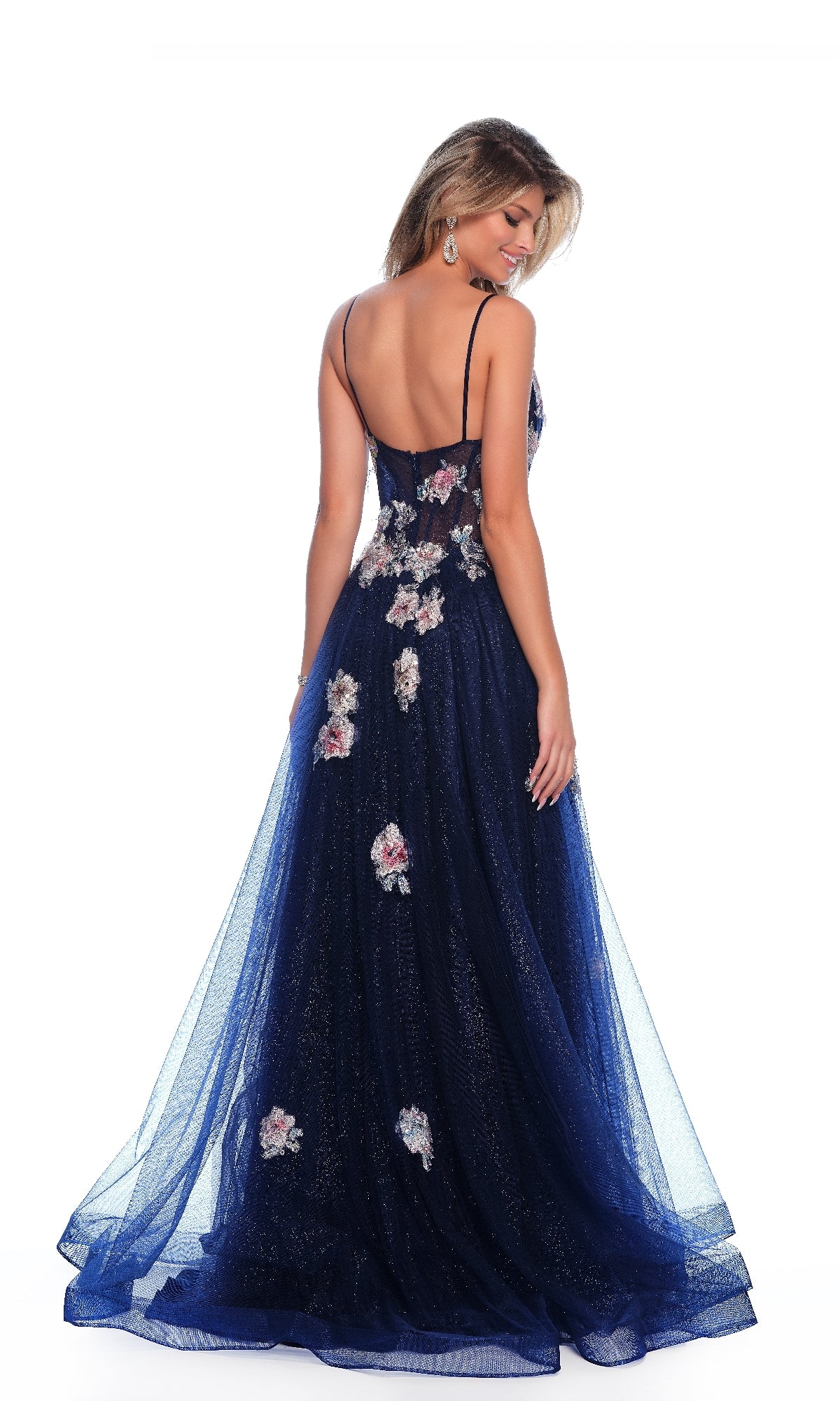 A woman stands facing away in a Long Prom Dress: Dave and Johnny 11870, featuring navy blue tulle, thin straps, and 3D flower embroidery that highlights the flowing a-line skirt.